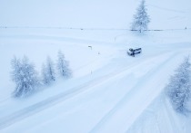 На снимке большой синий «Волгабас» стоит, накренившись, в сугробе снега за пределами проезжей части