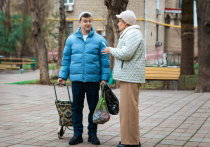 Филипп Бледный идет по московскому дворику с хозяйственной сумкой на колесах и пакетами с продуктами